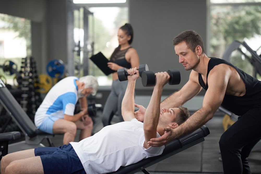 Dois homens na academia fazendo musculação com pesos