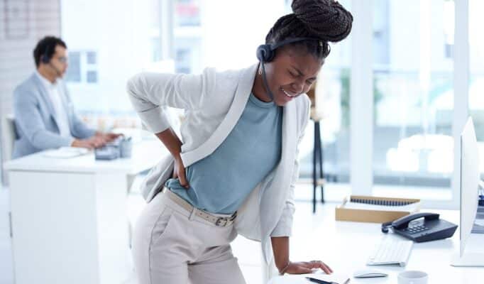 Foto de um jovem agente de call center com dores nas costas enquanto trabalhava em um escritório, ponto de tensão.